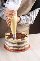 Confectioner at Work. Cream Cake Decorating. Cook Table Preparing a Tiramisu Cake on a Brown Background. photo