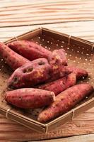 Red Sweet potato in a woven basket over rustic wooden background closeup photo