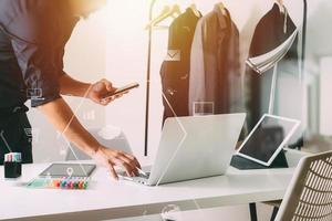 Fashion designer working with mobile phone and using laptop with digital tablet computer in modern studio photo