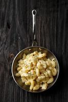 Creamy Macaroni and Cheese on a Skillet Oan with Parmesan and Herbs, Isolated on Wooden Table, Top View
