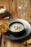 Mushroom Creamy Soup with Crispy Garlic Bread Baguette, Serve on Black Ceramic Bowl or Ramequin, on Rustic Brown Wooden Table. photo
