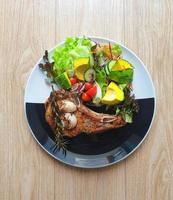 Grilled pork chop steak with salad on the black and white plate. Wooden table. Ketogenic or Atkins diet recipe. Low carb,high fat. Avocados is good fat. Fresh vegetables. Healthy food trend. Isolated photo