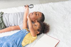 Happy sister and brother lying on floor with book, Children lying on floor with book and the magnifying glass photo
