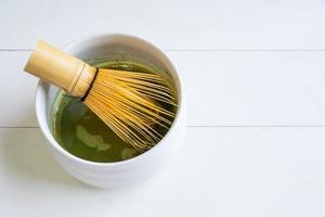mujer usando un batidor de bambú para mezclar polvo de té verde matcha con agua foto