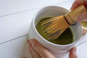 mujer usando un batidor de bambú para mezclar polvo de té verde matcha con agua foto