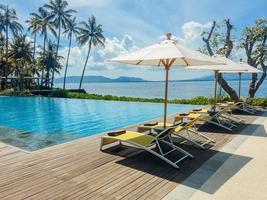 Beautiful tropical swimming pool in hotel or resort with umbrella, coconuts tree sun-loungers, palm trees with infinity pool view, ocean and mountain background. photo