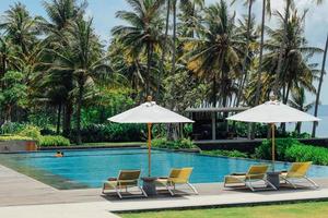 Beautiful tropical swimming pool in hotel or resort with umbrella, coconuts tree sun-loungers, palm trees during a warm sunny day, paradise destination for vacations