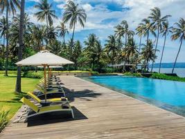 Beautiful tropical swimming pool in hotel or resort with umbrella, coconuts tree sun-loungers, palm trees during a warm sunny day, paradise destination for vacations