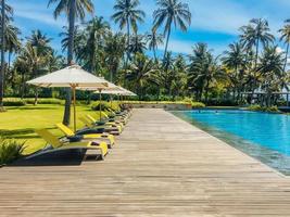 Beautiful tropical swimming pool in hotel or resort with umbrella, coconuts tree sun-loungers, palm trees with infinity pool view, ocean and mountain background. photo