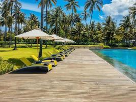 Beautiful tropical swimming pool in hotel or resort with umbrella, coconuts tree sun-loungers, palm trees during a warm sunny day, paradise destination for vacations photo