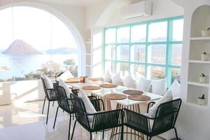 configuración de mesa y sillas de restaurante en el comedor con vista al mar desde la ventana foto