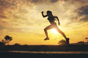 Silhouette of young woman start running at road track. Fit runner fitness runner during outdoor workout with sunset background. Selected focus photo