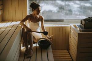 Young woman pouring water onto hot stone in the sauna