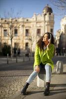 mujer joven escuchando música con un teléfono inteligente en la calle y tomando café para llevar foto