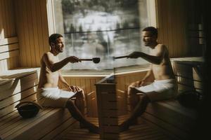 Young man pouring water onto hot stone in the sauna photo