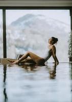Young woman relaxing on the poolside of infinity swimming pool at winter time photo