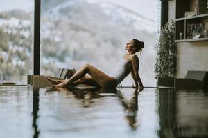 Young woman relaxing on the poolside of infinity swimming pool at winter time photo