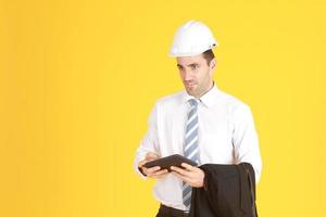 Handsome and smart engineer in suit and white shirt and Wearing a white safety engineer hat with hand holding smartphone isolated on yellow background. Copy Space photo