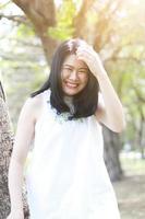hermosa mujer asiática con vestido blanco feliz y gran sonrisa con luz natural en el parque. niña tailandesa o niña china disfrutan de vacaciones en el jardín foto