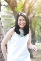 bella mujer asiática vestida de blanco relajada y sonriente en el parque natural. niña tailandesa o niña china disfrutan de vacaciones con la luz del sol en el jardín foto