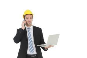 Handsome and smart engineer in black suit Wearing a yellow safety engineerking hat with hand holding labtop and call in mobile for work isolated on yellow background. Copy Space photo