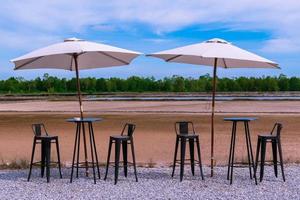 dos sombrillas con silla de hierro y mesa en el suelo de piedra con cielo azul y fondo de nubes entre la naturaleza en la cafetería. foto