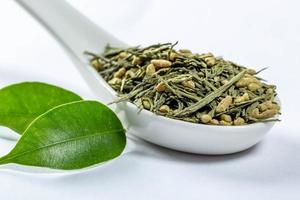 Green leaf tea with granules on a white ceramic spoon with fresh leaves photo