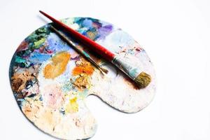Painter's palette with oil paint and brushes on white background