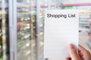 mano sosteniendo papel de lista de compras con estantes de tiendas de conveniencia foto