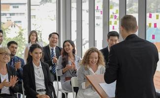 el grupo de audiencia de negocios de diversidad sonríe y escucha feliz al orador masculino dando un discurso en un evento de seminario corporativo en la sala de conferencias. foto