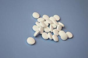 A bunch of simple tiny round white pills scattered on a blue background. Close-up, focus on one pill. The concept of medicine, nutritional supplements and drugs. Free space for text. photo