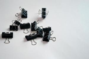 Black stationery clips randomly lying on a light background. Accessories for paper documents. Free space for text. photo