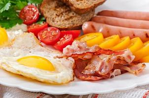 English breakfast - fried eggs, bacon, sausages and toasted rye bread photo