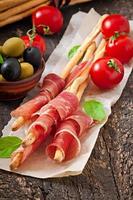 Grissini bread sticks with ham, olives, basil on old wooden background photo