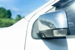 Close up side mirror wing of car  is foldable parking time. parking outdoor at day time. with blurred of trees under blue sky. photo