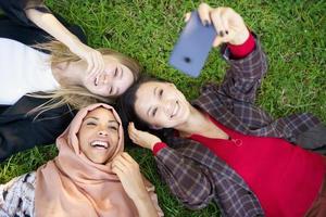 Cheerful diverse friends taking selfie on smartphone on grass photo