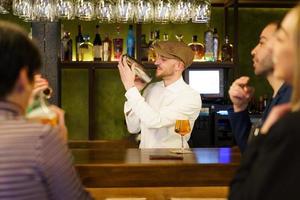 Positive barkeeper preparing cocktail for clients in a pub photo