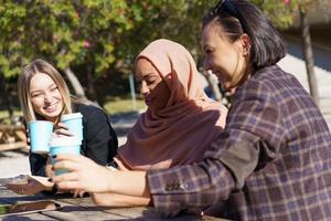 Happy multiethnic young women drinking takeaway coffee and smiling in park photo