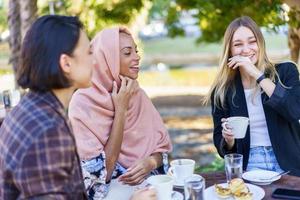 Laughing diverse female friends drinking coffee in outdoor cafe photo