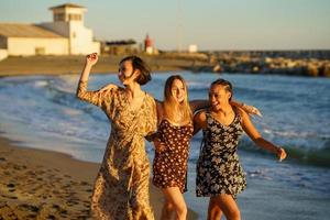 Happy diverse girlfriends walking on sandy beach photo