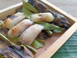 Grilled stuffed Glutinous rice wrapped in banana leaves or sticky rice with banana and taro on a wooden plate. Ancient sticky rice Thai style menu. Thai name is khao niao ping photo