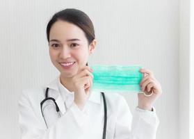 Asian beautiful young smiling female doctor is holding a mask to prevent contagious disease. Health and Corona virus concept. photo