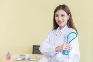 Young beautiful  Asian woman doctor Standing with arms crossed happy and smile in hospital. Wearing a white robe and stethoscope photo