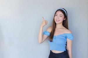 Young beautiful Asian woman is acting thumb up as a good symbol and another hand shows as presenting something on the background. photo