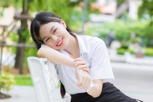 Portrait of adult Thai student in university student uniform. Asian beautiful girl sitting smiling happily at outdoors university with a background of outdoors garden trees. photo