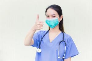 Young Asian female doctor wearing a medical mask is  showing hand as thump up on a white background. She wears a mask to protect her respiratory system Covid-19. photo