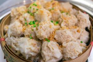 shaomai es una comida china que se hace con carne de cerdo encima con ajo frito y cebolleta picada puesta en una cesta de bambú. foto