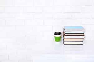Many books and a cup of coffee on white table near brick wall in the office. Copy space and selective focus photo