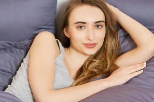 Good morning. Positive beautiful woman smiling at camera, lying in bed after good sleep photo