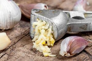 Close up of a garlic press and fresh garlic on old kitchen Board